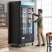 A man opening the black sliding glass door of an Avantco merchandiser refrigerator.