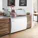 An Avantco ice cream dipping cabinet with a clear top on a counter with a man in a white apron.