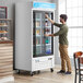 A man opening an Avantco white sliding glass door refrigerator.