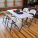 A white Lifetime light duty folding chair on a table with food and three other chairs.