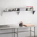 A Regency stainless steel wall shelf holding food containers above a stainless steel counter.