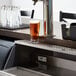 A Regency stainless steel underbar mount beer drip tray on a counter with a glass of beer.