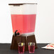 A Tablecraft brown plastic beverage dispenser with pink liquid and lime slices in a glass.