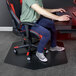 A man sitting at a desk using a computer with an ES Robbins black vinyl chair mat.