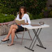 A woman sitting in a chair reading a book at a Lifetime almond folding table on an outdoor patio.