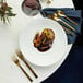 A white plate with food next to a Oneida Chef's Table gold butter knife.