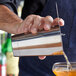 A bartender using an Arcoroc stainless steel bar shaker to pour a cocktail.