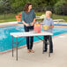 A woman and a boy standing next to a Lifetime plastic folding table with fruit on it.