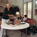 A woman serving food on a Lifetime plastic folding table in a living room.