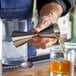 A person using an Arcoroc stainless steel Japanese style jigger to pour liquid into a glass.