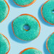 A group of donuts with green frosting and Adourne Light Green Sanding Sugar on top.