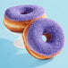 Two purple donuts with Adourne lavender sanding sugar sprinkles on a white plate.