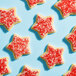 A group of star-shaped cookies topped with fine red sanding sugar on a light blue background.