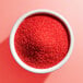 A white bowl filled with fine red sanding sugar.
