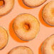 A group of donuts coated with fine orange sanding sugar on an orange background.