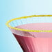 A pink cocktail with a yellow Adourne Sanding Sugar rim on a table.