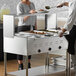 A man and woman serving food from a ServIt electric steam table at an outdoor catering setup.