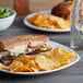 A plate with a sandwich, jalapeno kettle-cooked potato chips, and a pickle next to a bottle of water on a table in a deli.