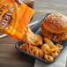 A hand pouring Martin's Bar-B-Q Pork Rinds into a burger with fried onion rings.