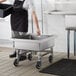 A man in a black apron using a Regency mobile silverware soaking sink on a counter.