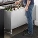 A man standing next to a Regency stainless steel beer box filled with bottles of beer.