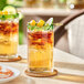 Two Acopa Tropic cooler glasses filled with a green drink, ice, and fruit on a table.