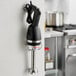 A black and silver Galaxy 9" light-duty immersion blender on a wall mount over a counter in a professional kitchen.