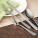 A close-up of a Walco medium weight stainless steel salad fork on a table with other silverware.