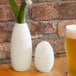 A white Front of the House bud vase with a flower next to a glass of beer.