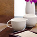 A white table with a white cup and Front of the House white porcelain creamer on it.