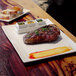 A plate of food with a piece of meat and sprigs of herbs on a white rectangular plate.