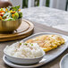 An Artefact porcelain oval plate with food and a bowl of salad on a table.