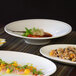 A table in a farm-to-table restaurant with a group of white porcelain spiral flare bowls filled with food.