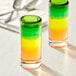 A close-up of two Acopa Tropic shooter glasses with green, yellow, and red liquid.