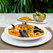 A white porcelain plate with seafood soup, salad, and seafood.