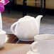 A white Front of the House porcelain teapot on a white surface with a white cup.