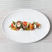 A white Front of the House oval porcelain coupe plate with food on it.