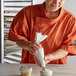 A woman in an orange shirt using an Ateco reusable pastry bag to frost a cupcake.