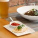 A Front of the House white rectangular porcelain plate with food and a glass of beer on a table.