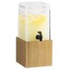 A Cal-Mil bamboo beverage dispenser on a wooden base with a black tap filled with lemonade.