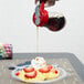 A person using a Tablecraft glass syrup dispenser to pour syrup on a plate of food.