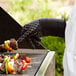 A person wearing Outset oven gloves cooking food on a grill.