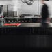 A man using a Vollrath red cutting board on a counter in a professional kitchen.