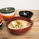 A green Front of the House oval porcelain bowl filled with ramen noodles, egg, and vegetables on a table.