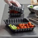 A person in plastic gloves using an Ecopax black plastic take-out container to prepare food.