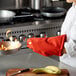 A woman in a white coat and orange gloves using a San Jamar oven mitt to hold a flaming pan.