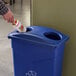 A person putting a bottle into a blue Carlisle recycling bin with a rectangular lid.