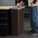 A man putting a coffee cup in a Carlisle brown rectangular trash can.