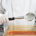 A person using a Vollrath Jacob's Pride black solid oval spoodle to serve food.