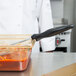 A person in a white coat using a Vollrath Black Solid Oval Spoodle to serve red sauce.